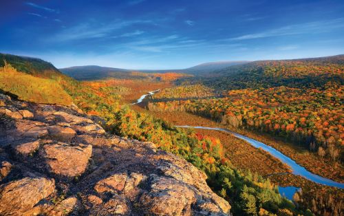 The image is of Carp River Valley. There are beautiful trees with a view of the river from above flowing down.